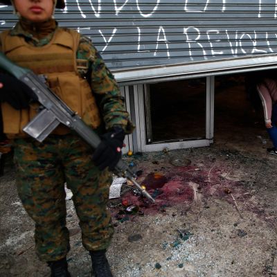 En soldat övervakar ett vandaliserat köpcenter i Santiago. Åtminstone 40 köpcenter och andra företag plundrades på söndagen, enligt det chilenska inrikesministeriet. 