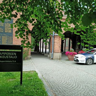 Pirkanmaan käräjäoikeuden rakennus ulkoa kuvattuna. Talon edessä poliisiauto.