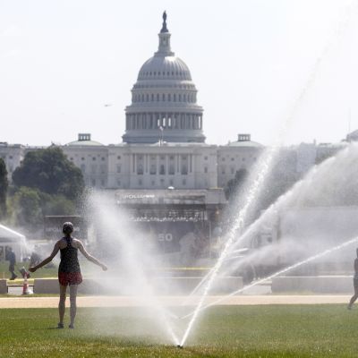 Två kvinnor svalkar sig under vattenspridare på gräsmattan framför Kapitolium i Washington DC under en extrem värmebölja i juli 2019.