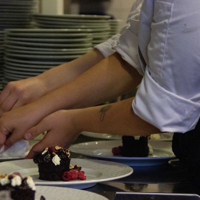 Många handpar hjälper till att rätta till små efterrätter av choklad i ett storkök.