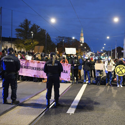 Poliisit ja Elokapinan mielenosoittajat ovat vastakkain Eduskuntatalon edessä iltapimeällä.