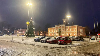 Bilar står parkerade på ett snöigt och slaskigt torg. På torget står en stor julgran och i bakgrunden är ett ståtligt ljusrött hus, Lovisa stadshus.