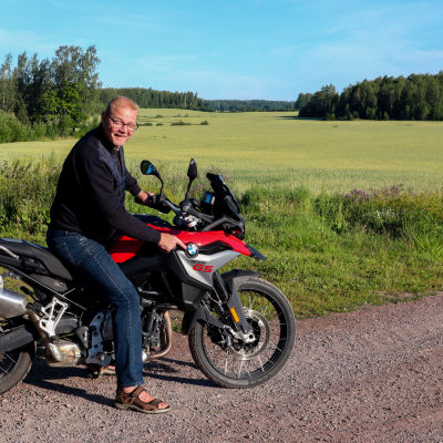 En man sitter på en motorcykel framför en åker.
