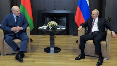 Aleksandr Lukasjenko och Vladimir Putin sitter bredvid varandra och tittar på varandra. I bakgrunden syns ländernas flaggor.