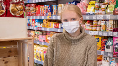 En ung kvinna med vitt munskydd står inne i en affär.