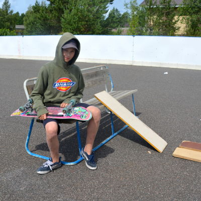 En pojke sitter på en bänk med en skejtboard i famnen. 