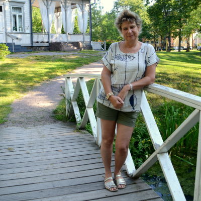 En kvinna står på en vit träbro i en park. 