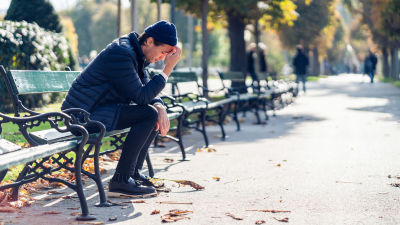 Ung man sitter på en bänk i höstsolen och ser utmattad ut
