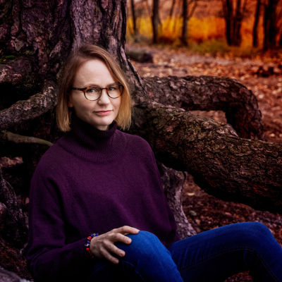 Författaren Maria Grundvall sitter i skogen.