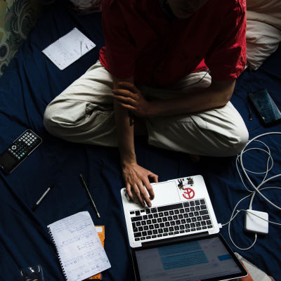 En ung studerande sitter i sängen och studerar.