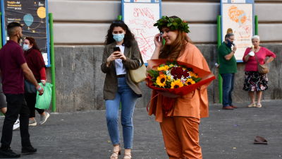 En ung kvinna i orange sidenkostym håller en stor bukett blommor i handen. Hon har också en bladkrans på huvudet.