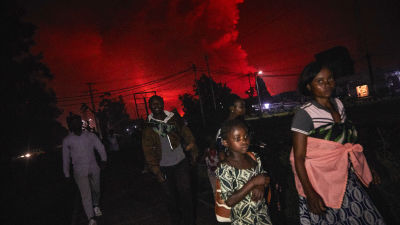 Kongoleser med packning flyr undan vulkanen Nyiragongos utbrott. Himlen bakom dem är färgad röd av utbrottet.