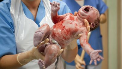 en otvättad nyfödd baby som barnmorskan håller upp