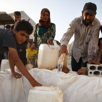 Syrier som är på flykt i inne i Syrien fyller kanistrar med vatten.