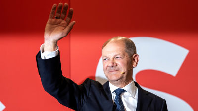 Olaf Scholz vinkar och ler medan han tittar åt sidan.