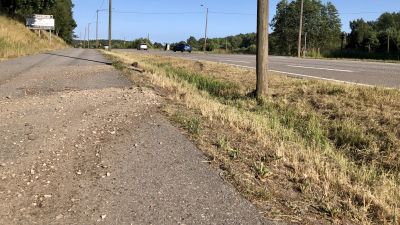 Sand och grus på asfalten på en gång- och cykelväg invid en bilväg. Sommar, solen skiner, ett par bilar syns på vägen.