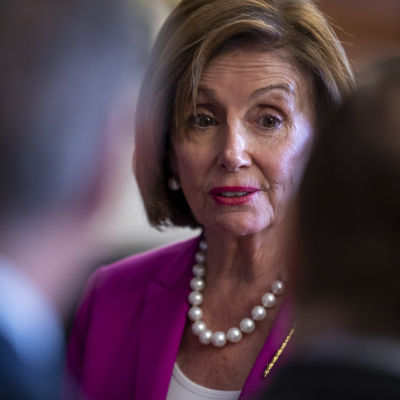 Nancy Pelosi tittar fram mellan två mörkklädda män i förgrunden.