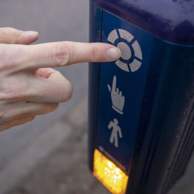 En hand trycker på knappen för trafikljuset vid ett övergångsställe. 