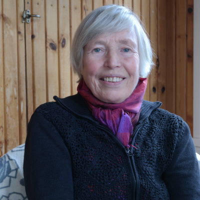 Anita Österberg sitter framför en brun träpanel