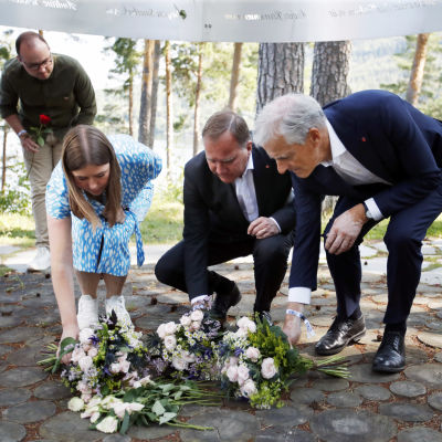 Kolme henkilöä asettelee kukkia maahan muistotilaisuudessa.