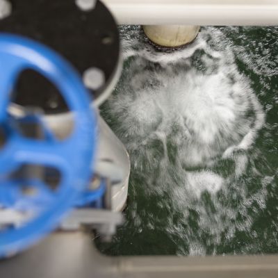 Bild på vattenrening. Vatten rör sig i en bassäng i ett reningsverk så det bildas vitt skum.