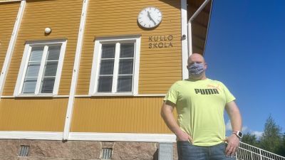 En man i gul t-skjorta står framför ett vitt trähus där det står Kullo skola.