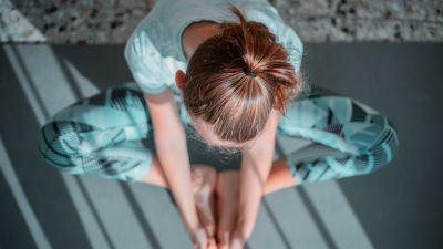 En kvinna i träningskläder sitter på en yogamatta och tänjer.