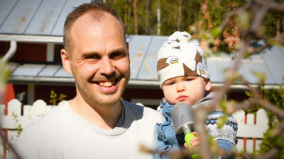 Martin Norrgård med sonen i famnen i vårsolen hemma på gården