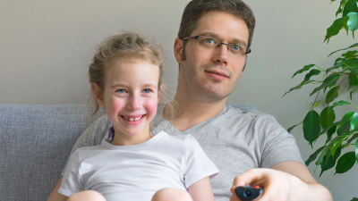 Pappa och dotter sitter på soffan och tittar på tv.