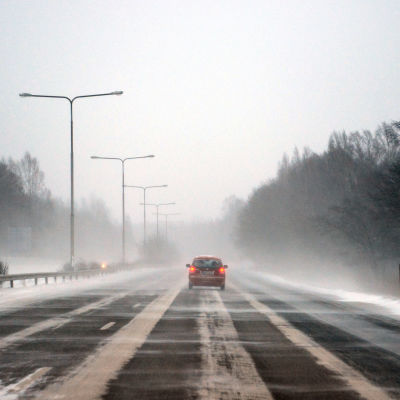 En bil kör på en motorväg, snön yr.