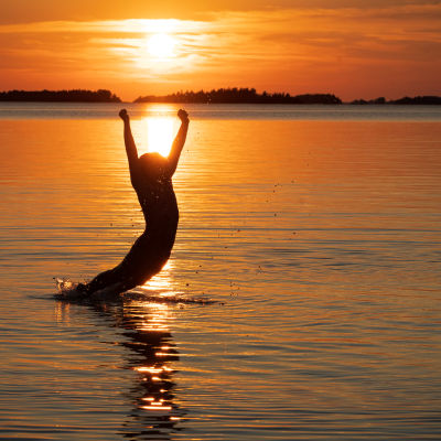 Tyttö hyppää uimaan mereen auringonlaskun aikaan.