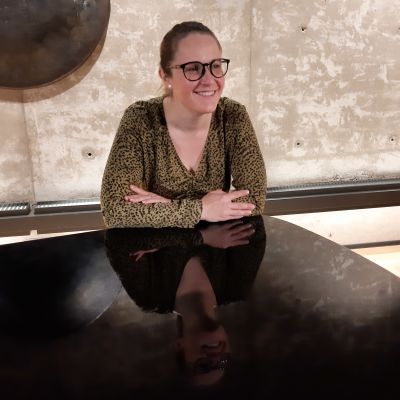 Anna Törnroos-Remes, en dag med glasögon och håret bakåtkammat i en knut, lutar sig mot en flygel.