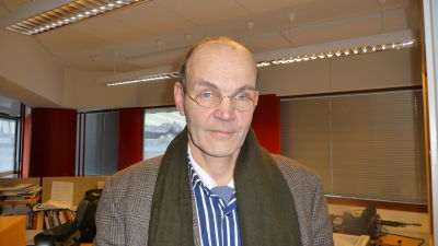 En man står i en kontorsmiljö. Han har en neutral min och ser in i kameran.