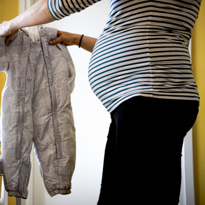 Gravid kvinna håller i en babyoverall.