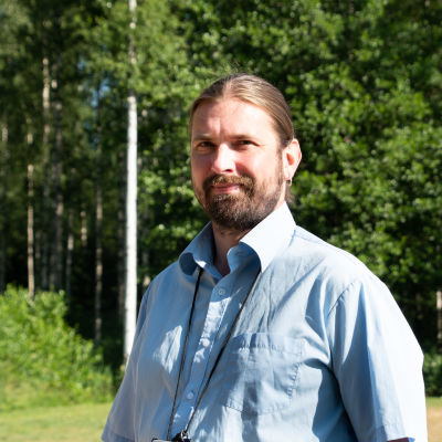Kristian Meurman i ljusblå skjorta i solsken med lövträd i bakgrunden. 