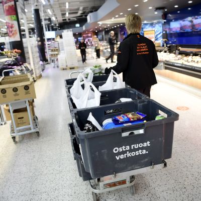 En person i citymarket-uniform drar en kärra med matlådor inne i en matbutik.
