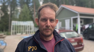 Mansperson står ute på egnahemsgård. I bakgrunden syns bilar parkerade och ett växthus.