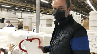 Bild på Peter Nordlund, iklädd svart munskydd tillverkat i hans fabrik. Han håller i ett kassettfilter och står inne i den fabrikshall som tillverkar dem.