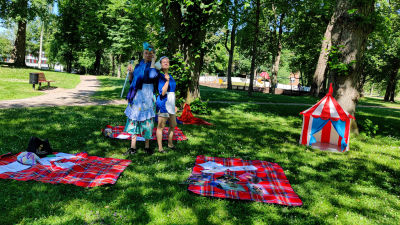 En man och en kvinna utklädda till städerskor står i en lummig park.