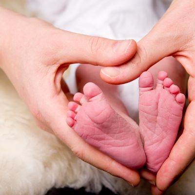 nakna babyfötter. En vuxen människas händer formade till hjärta runt de här små babyfötterna.