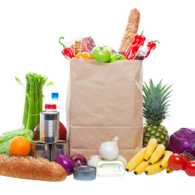 En brun papperskasse med olika matvaror, fotograferad från sidan. 