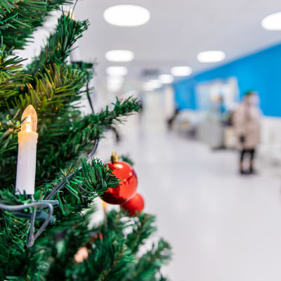 Joulukuusi jossa kuusen kynttilä sairaalan käytävällä. taustalla asiakkaita.