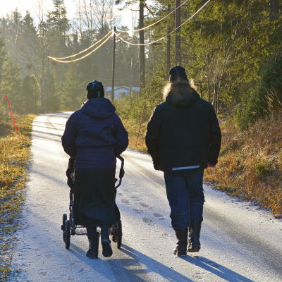 Kvinna och man promenerar med barnvagn på en frostig väg.