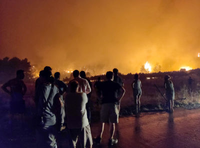 Flera människor står och tittar på en skogsbrand i Limni i Grekland.