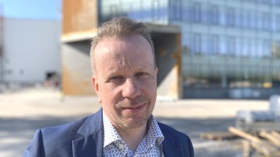 Mansperson i blå skjorta och kavaj står framför nybyggd kontorsbyggnad.