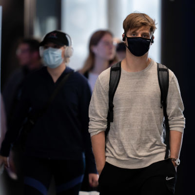En ung man kommer gående mot kameran med munnen och näsan täckt av ett munskydd.
