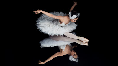 Tanssija Hanako Matsune valkoisessa joutsenasussa mustalla, peilipintaisella esiintymislavalla. Kuva Kansallisbaletin Joutsenlammesta.