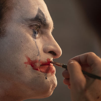 Närbild då Arthur (Joaquin Phoenix) sminkar sig till clown samtidigt som han gråter och blå mascara rinner nerför kinden.
