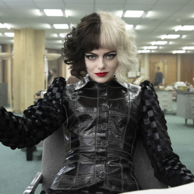 Närbild på Cruella (Emma Stone) som sitter och ser klurisk ut.