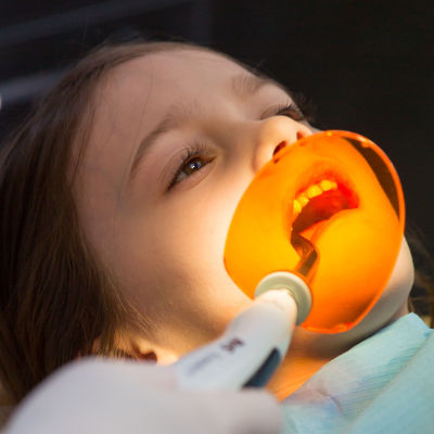 En flicka ligger i tandläkarstolen med tandläkarinstrument i munnen.